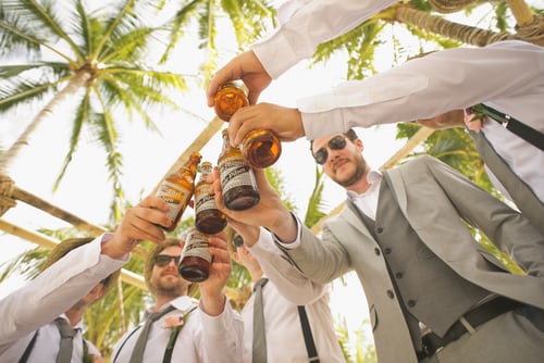 groom team sous les palmiers trinquant avec une bière lors d'un mariage à l'étranger