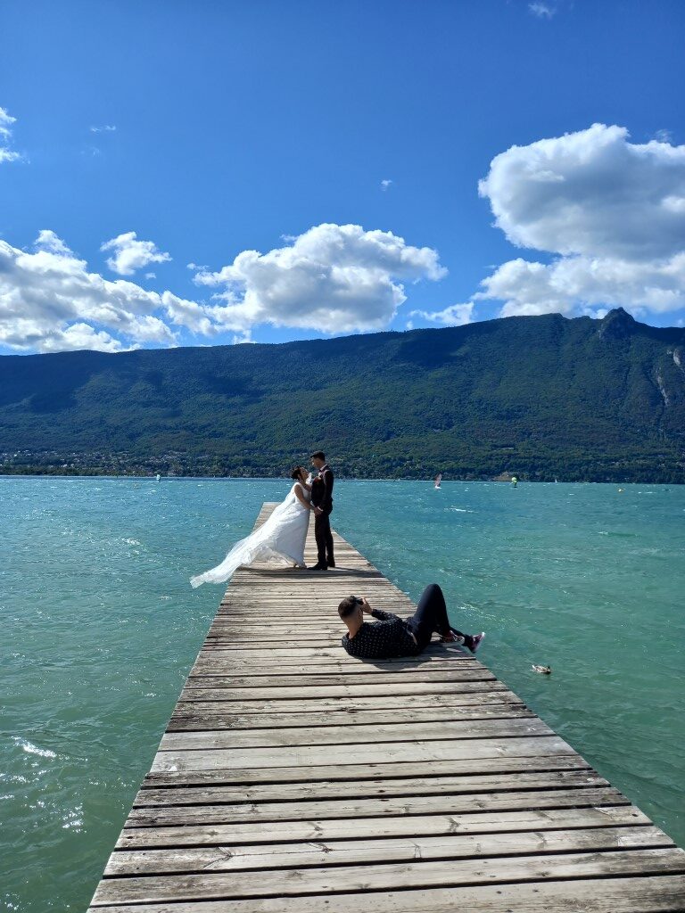 photographe allongé sur un ponton pour prendre en photo des mariés sur le lac du bourget